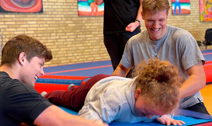 tre unge laver gymnastik på en måtte og griner sammen