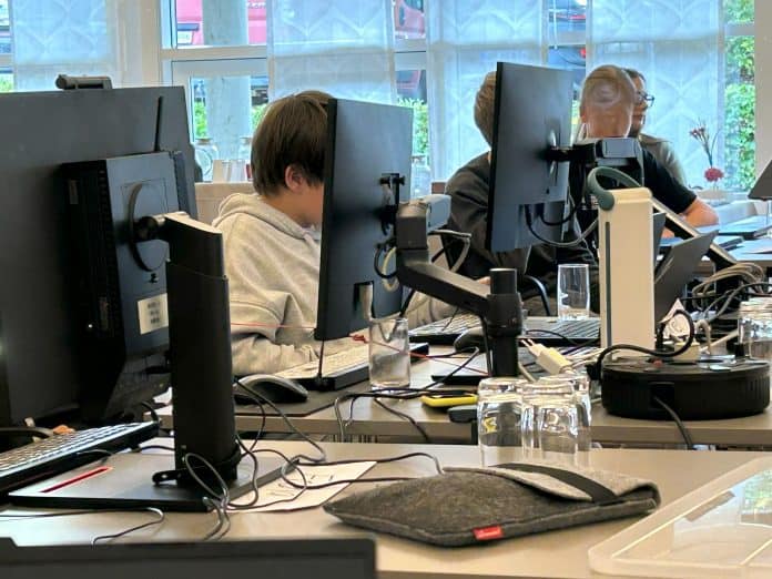 PC-camp skærme Bord med store computerskærme, hvor tre unge sidder ved siden af hinanden og arbejder
