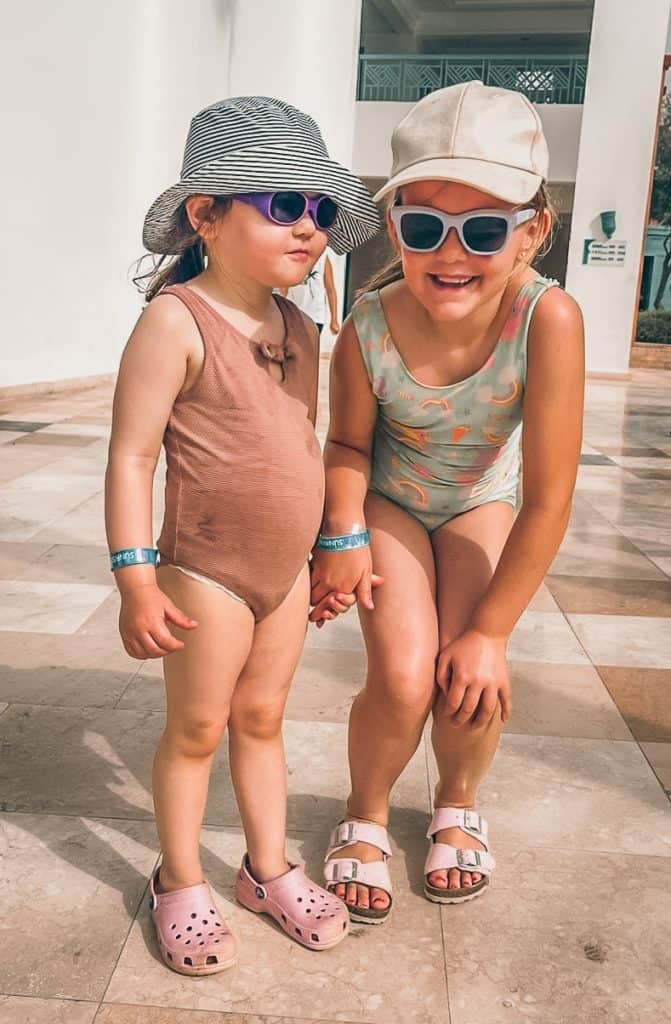 Lykke og Karla står side om side på deres sommerferie i Egypten, iført badetøj, solbriller og solhatte under den klare sol