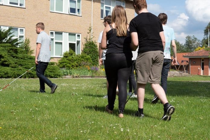 En gruppe unge med blindestok går over græsplænen ved efterskolen på Synscenter Refsnæs