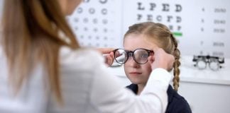 Øjensygdomme hos børn En pige sidder foran øjenlægen og prøver et par briller med ny styrke