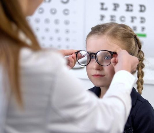 Øjensygdomme hos børn En pige sidder foran øjenlægen og prøver et par briller med ny styrke