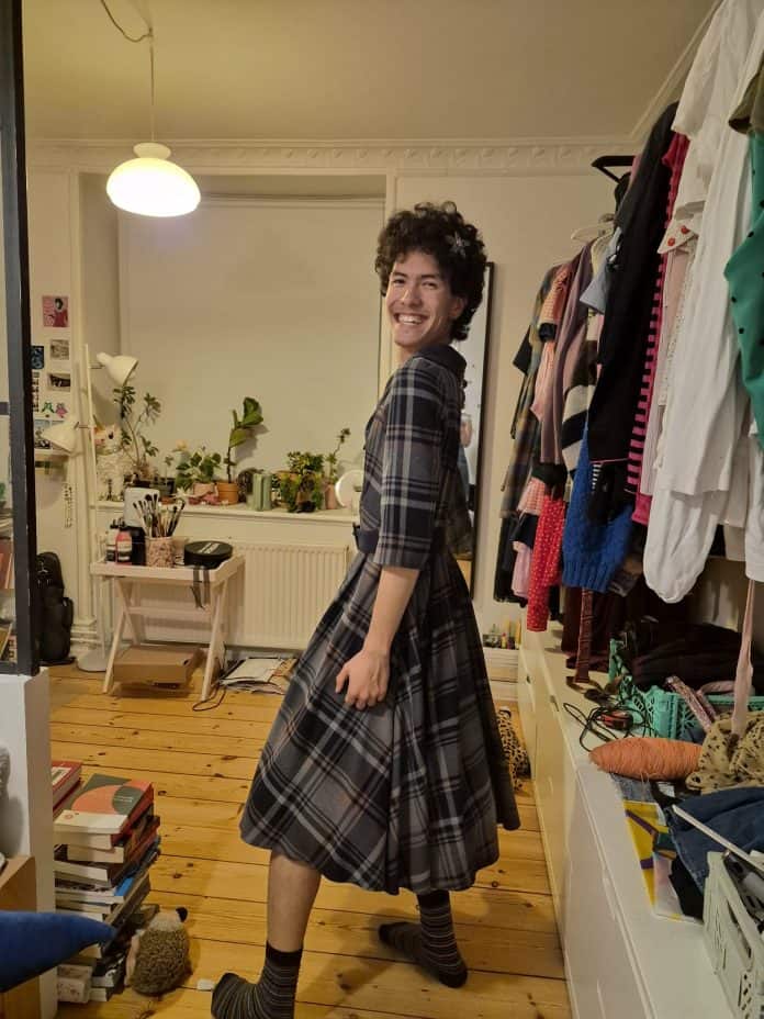 Tor Pogan prøver en ternet, grå kjole på sit værelse ved siden af en fyldt garderobestang