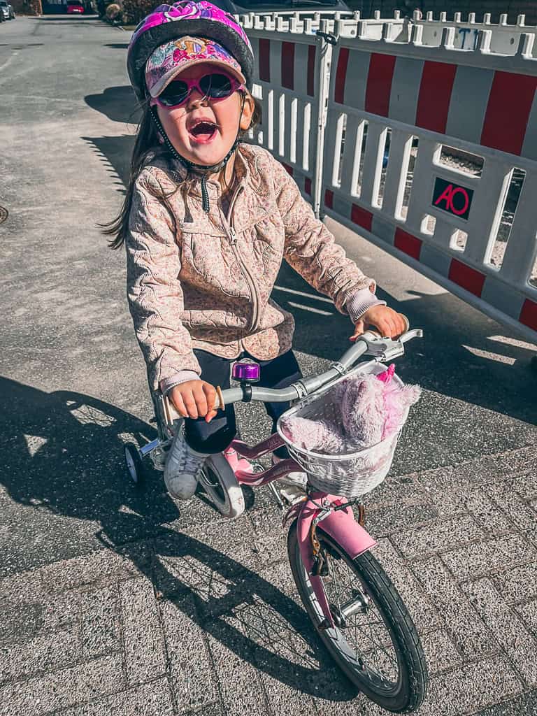 Et af påskens projekter var at lære Lykke at cykle på pedalcykel. Her på billedet er hun godt på vej iført cykelhjelm, kasket og mørke solbriller.