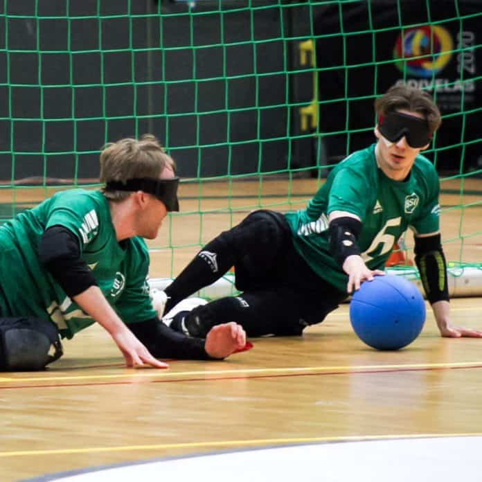To goalballspillere på gulv med blændede øjne og en blå bold