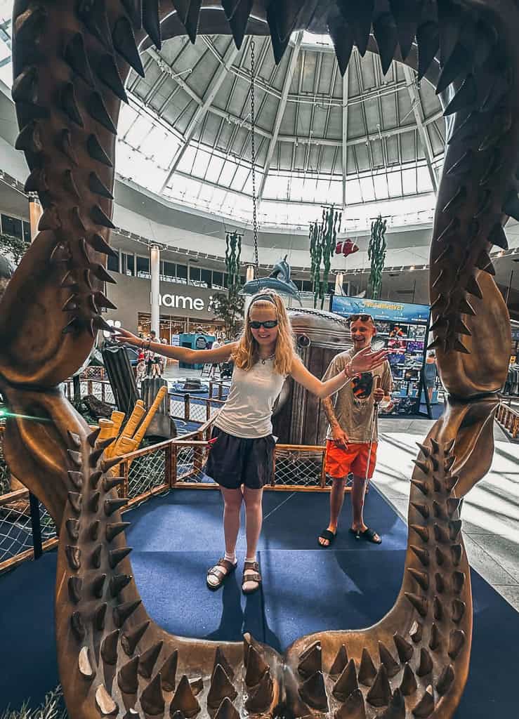 Elina st&aring;r foran et stort dinosaurskelet, hvor k&aelig;berne danner en bue om hende. 