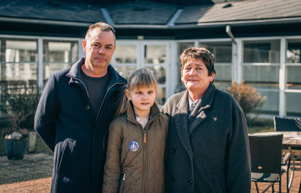 Elina st&aring;r mellem sin morfar, Michael, til venstre og sin mormor, Anja, til h&oslash;jre. Hun er i netv&aelig;rkspleje hos dem. 